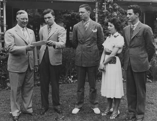 Robert Stilz, Lexington, President of the 1938 graduating class of the University of Kentucky, shown presenting to Marcus C. Redwine (left), Winchester, President of the University Alumni Association, a check representing 100% membership of the class in the organization.  At Stilz's left are Rankin Terry, Marion, Vice-president of the class; Mary Lou Stark, Lexington, class secretary, and Leon McCrosky, Harrodsburg, class treasurer; the location in Maxwell Place, the home of University President Frank L. McVey, where today he and his wife were hosts to several hundred graduates, faculty and friends of the University at their annual senior breakfast; taken from Lexington Herald-Leader