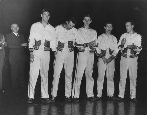 Coach Adolph Rupp at left standing and clapping and members of the [1946-47] basketball team; pictured left to right are Wallace Jones, unidentified, Joe Holland, Ralph Beard, and Kenny Rollins