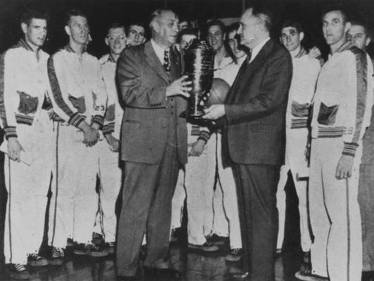 Basketball coach Adolph Rupp (right) and 1947-48 basketball team accepting the NCAA Championship trophy (players left to right: Jim Line, Dale Barnstable, John Stough?, Joe Holland, Alex Groza [obscured], Ralph Beard [obscured], Wallace 