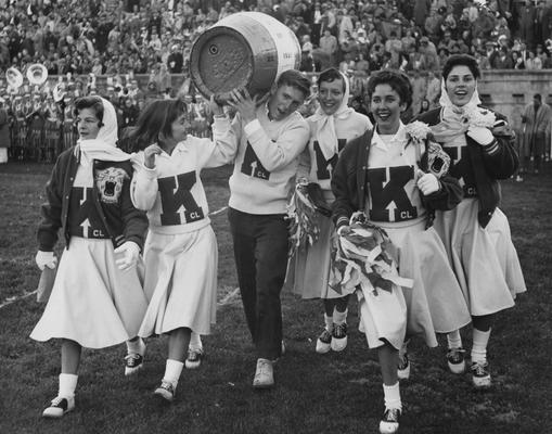 Cheerleaders with bobbie socks and saddle oxford shoes attending the homecoming football game at Stoll Field, November 23, 1957; pictured from left to right are Nancy Lowe, Pat Nallinger, Ellery 