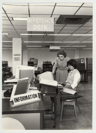 Norma Jean Gibson (woman standing with glasses), reference librarian, helps a female student in the Reference Area on the first floor of the Margaret I. King Library; This image was submitted for use in the 1983 / 1984 O. C. L. C. Annual Report