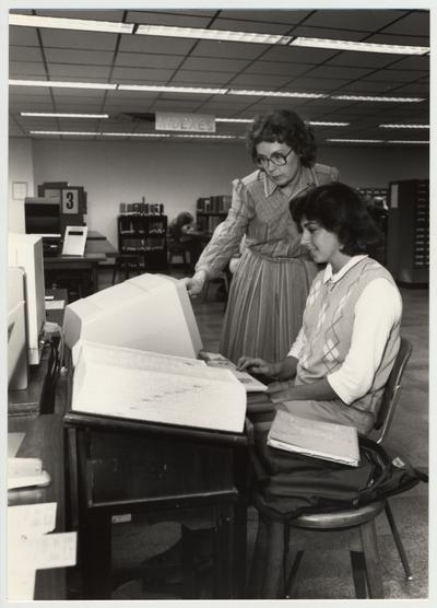 Norma Jean Gibson (woman standing with glasses), reference librarian, helps a female student in the Reference Area on the first floor of the Margaret I. King Library; This image was submitted for use in the 1983 / 1984 O. C. L. C. Annual Report