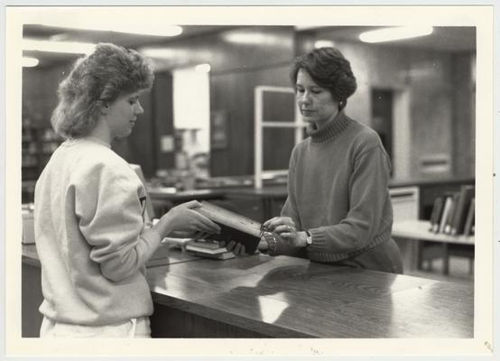 A student hands a book to librarian Judy Brown (right)