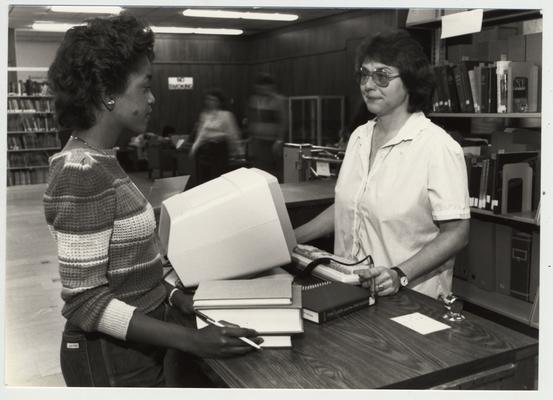 A student checks out a book from the library; Submitted for use the the 1983 / 1984 annual Report