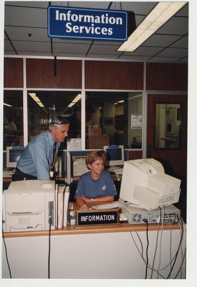 A man and woman look at a computer behind the Information Services desk in the Medical Library (located in the Medical Center); Photographer: Mark Minor
