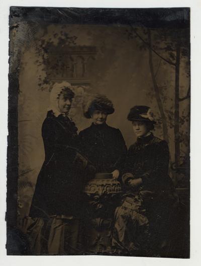 Three women dressed nicely posing for a picture.  Tintype
