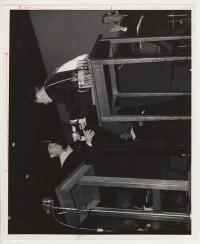 President Frank Dickey is standing in cap and gown and is presenting a document to an unidentified person at Frank Dickey's inauguration ceremonies