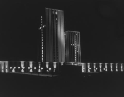 A color photo of the Kirwan-Blanding Complex at night, with the windows of the towers lit-up in the shape of a cross