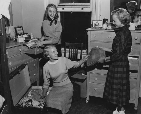 Three women either packing or unpacking a trunk. From left to right: Jerry Kelley, Betty Clay, and Benita Boyd. During the 1950's upper-class women had a curfew of 10:30p.m. on the weekdays and 11p.m. on the weekends. Photographer: Lexington Herald-Leader