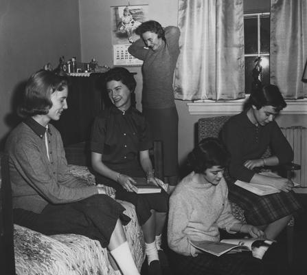 From left to right: an unidentified woman, unidentified woman, Betty Jane Mitchell (standing), Judy Goodall, and Linda Mount (in chair) are socializing in a dorm room. Received January 14, 1959 from Public Relations