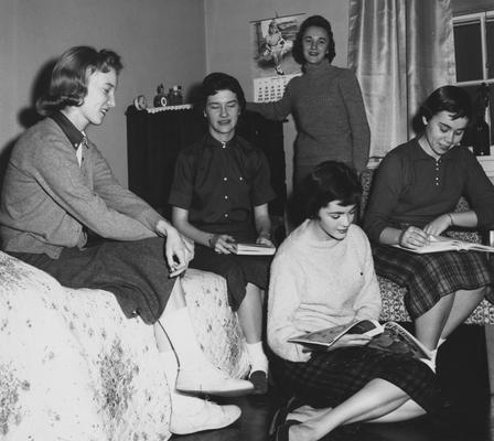From left to right: an unidentified woman, unidentified woman, Betty Jane Mitchell (standing), Judy Goodall, and Linda Mount (in chair) are socializing in a dorm room. Received January 14, 1959 from Public Relations