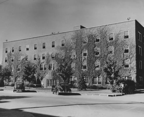 Cars parked in front of Jewell Hall, a women's residence hall, and an unidentified woman is entering the building. Jewell Hall was named after Mary Frances Jewell. Photographer: W. E. Sutherland
