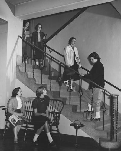 Two unidentified women are seated by stairs and four unidentified women are going up and down stairs in Jewell Hall. Jewell Hall was named after Mary Frances Jewell. Received March 16, 1957 from Public Relations