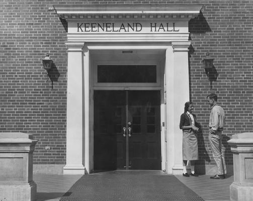 Ann Shirley Gillook (Miss Kentucky 1957) is talking to a young man at the entrance of Keeneland Hall, a woman's dorm. Keeneland Hall was named after the Keeneland Foundation which donated $200,000 and on October 17, 1955, it was dedicated to the foundation. This photo appears on page 22 of the 1956-1957 