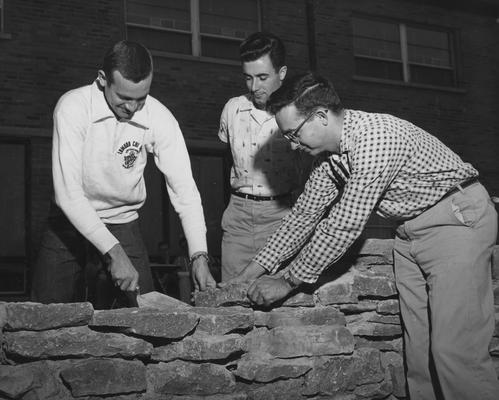 Three unidentified men are constructing a stone wall