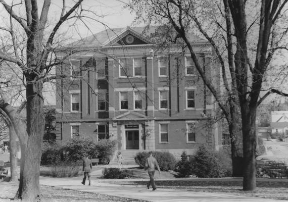 Unidentified people walking by Frazee Hall. Frazee Hall was built in 1907 and named after David Frances Frazee on June 3, 1931. On January 24, 1956, the building was partially destroyed by a fire. Photographer: John Sutterfield