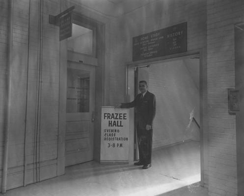 An unidentified man is is standing beside a sign by Frazee Hall. Frazee Hall was built in 1907 and named after David Frances Frazee on June 3, 1931. On January 24, 1956, the building was partially destroyed by a fire