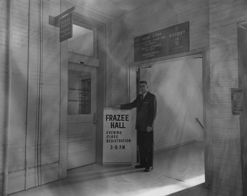 An unidentified man is is standing beside a sign by Frazee Hall. Frazee Hall was built in 1907 and named after David Frances Frazee on June 3, 1931. On January 24, 1956, the building was partially destroyed by a fire