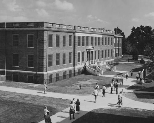 Unidentified students are walking past the Journalism Building. The Journalism Building was dedicated on November 2, 1951 and named after Enoch Grehan. It is also the home to the independent student newspaper, 