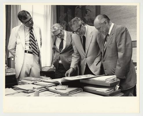 President Singletary is standing and looking at an oversized book.  From the left:  Dr. Hornback, University of Kentucky Vice President; Charles Thomas; President Singletary; and Earl Wilson Sr., Board of Trustees Member and Vice President of Central Bank, Lexington and Kentucky Insurance Company.  The title of the book is 