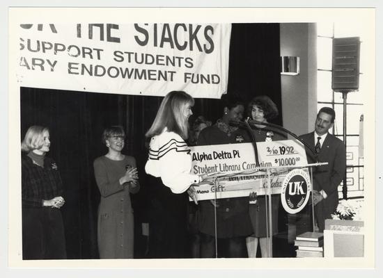 Unidentified women of Alpha Delta Pi are giving an oversized check for 10,000 dollars to the Student Library Campaign