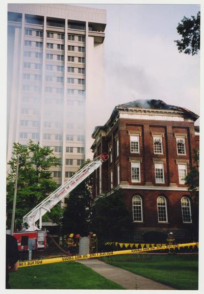 Unidentified fire fighters are standing outside of the Administration / Main Building putting out the fire