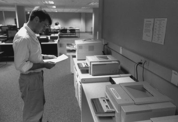 An unidentified man is standing at printers in the computer lab