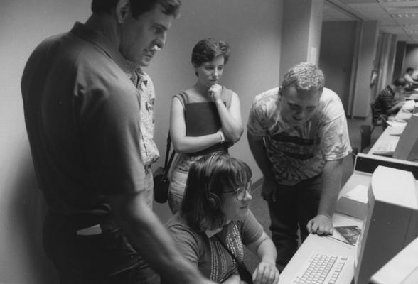 Five unidentified people are looking at a computer in the computer lab