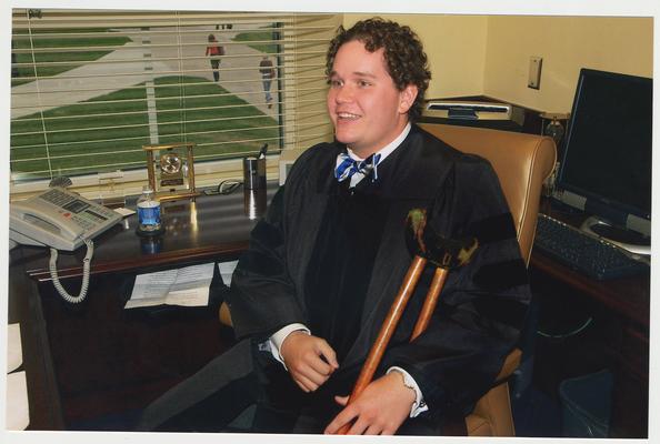 A UK student actor is portraying First President James K. Patterson of UK.  He is in President Todd's office.  It is part of a ceremony for the reopening of the Main Building