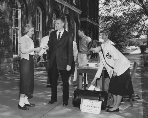 Alexander is handing a card to a woman trying to get her to vote for him as Commerce Representative