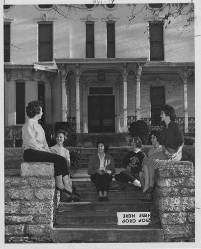 Six women talking outside the Hamilton House. From left to right: unidentified, Linda Lloyd, unidentified, Patricia Hager, unidentified, and Carole Ward. This photo appears first on page 241 in the 1963 Kentuckian
