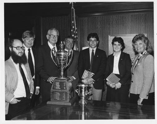 Debate Team left to right: Two unidentified men, UK President Otis Singletary, Harry Snyder, attorney and head of the Council on Higher Education, David Brownell, debate team member who won the national debate tournament, Ouita Papka, the first woman to win the national debate tournament and Governor of Kentucky Martha Layne Collins congratulating the UK student participants