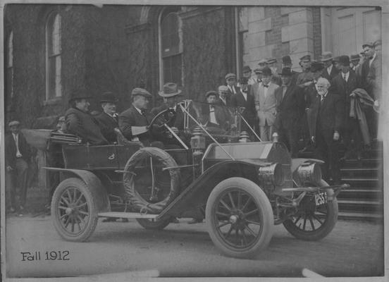 Red Oldsmobile parked in front of the University of Kentucky Administration Building; Driving: Dean F. Paul Anderson; Backseat: William Jennings Bryan and University of Kentucky President Henry B. Barker; University of Kentucky faculty members stand on steps in the background (bearded man on bottom left is University of Kentucky Vice - President and Professor of English James Garrard White)
