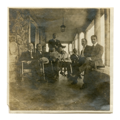Group portrait of unidentified people on a porch.  Handwritten on verso, 