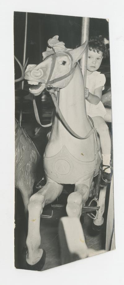 Little girl on carousel horse, amusement attraction, Joyland Park - stamped on back of photograph MACK HUGHES PHOTOGRAPH 503 E. HIGH LEXINGTON, KY