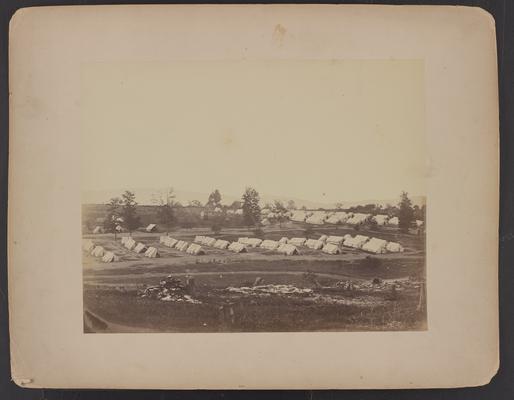 Camp Nelson convalescent camp; eight rows of four white tents each, small group of people sitting in front of them, trees and more tents in background, cleared area and tree stumps in foreground, written on back in pencil, upper left corner, Harmsfeld (?) No 2, on lower left 8 Phelps 3a (?)