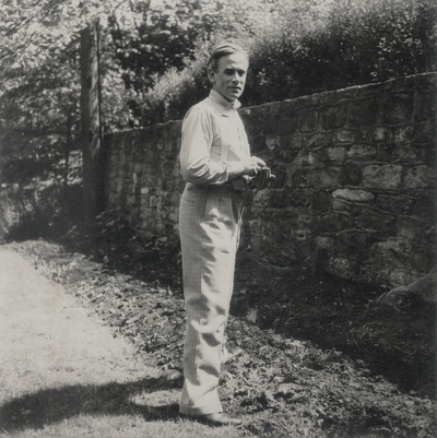 John Jacob Niles standing by a stone wall; Richmond, Virginia