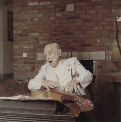 John Jacob Niles performing in front of fireplace; Boot Hill Farm