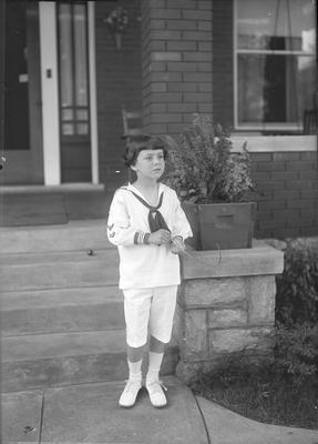 a child standing on the front walkway holding a stick (appears to be the same child as in item #6,7,10, and 11)