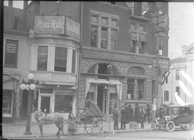 Versailles, exterior of Citizens National Bank, storefronts on either side, people on the street in front