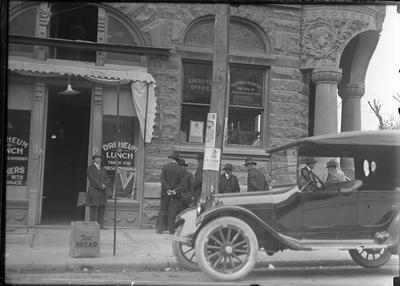 Sheriff's Office and a restaurant on a corner, people standing around outside, possibly in Versailles