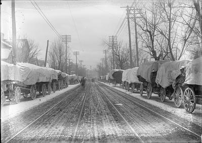 wagons that appear to be filled with crops and covered with tarps line the street