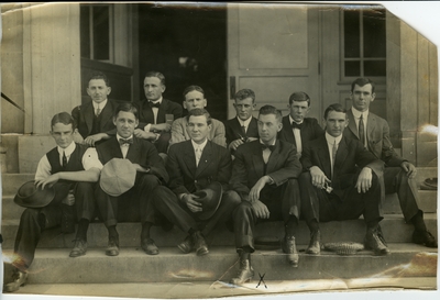 Group of 11 men seated on the steps of a building circa 1914