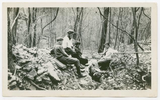 A group of four young women and two young men sitting on a stones in a forest