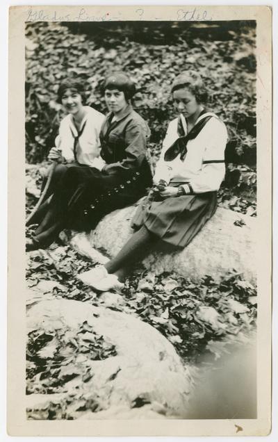 Gladys Lowe, ?, Ethel [sitting on a rock with leaves in the foreground and background] down on Kentucky River camping, 1919-1923.  Two of the women are wearing sailor shirts and bloomers