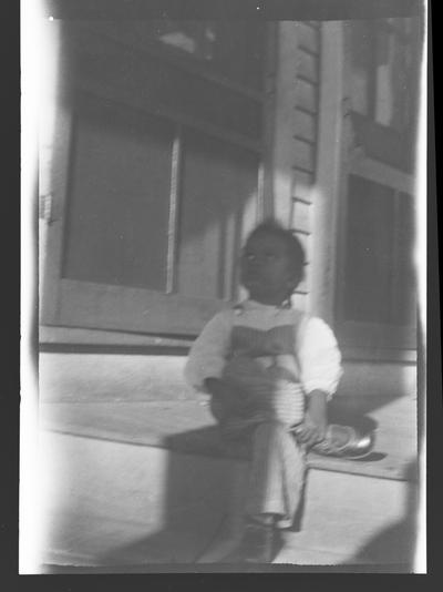 Negative of unidentified child sitting on steps