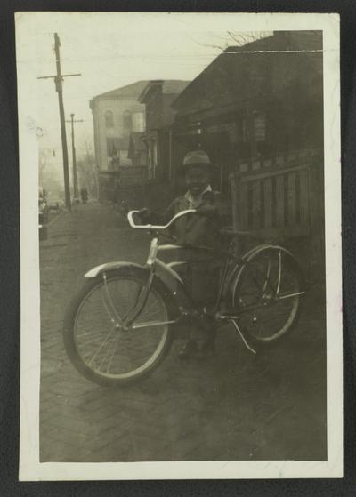 Master Chas. [Charles] Edward Bass taken in front of his mother's house on Cedar St. with his wheel. Age 6