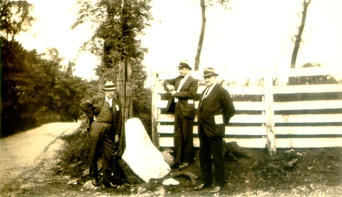 Three men standing by a fence