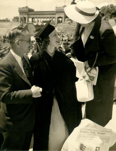 Young woman in academic robe with a man and woman, probably at college commencement. (Syracuse Daily Orange newspaper is visible)