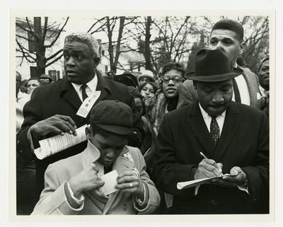 Dr. Martin Luther King, Jr., taking notes during march, Jackie Robinson to his left